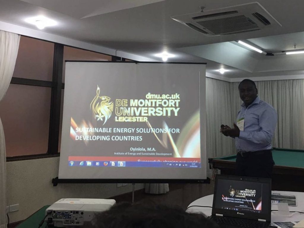 A man lecturing beside a large screen